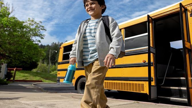 Young boy holding a FUNtainer Water Bottle walking away from a school bus