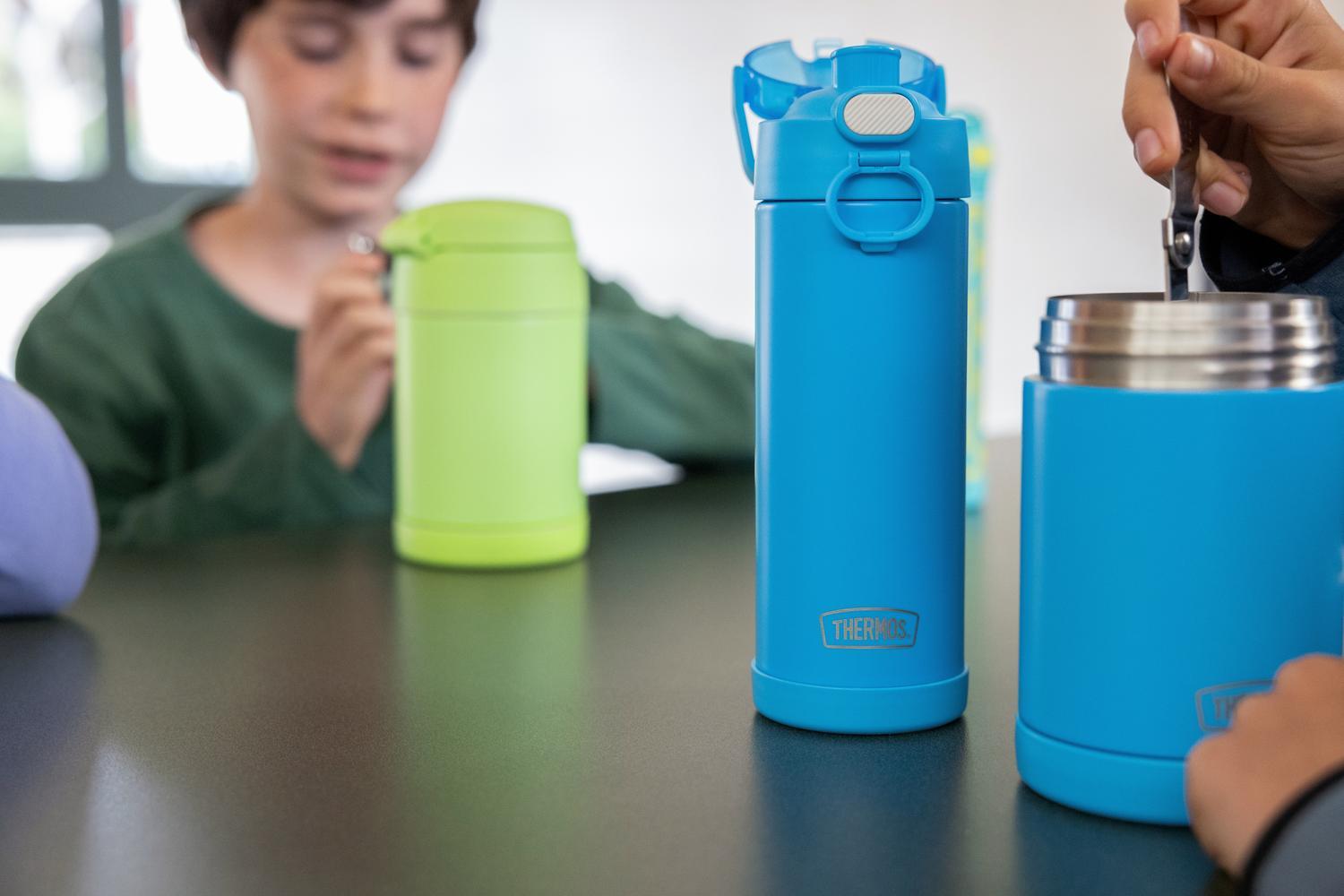 Children with blue and green thermos bottles and food jar on a lunch table.