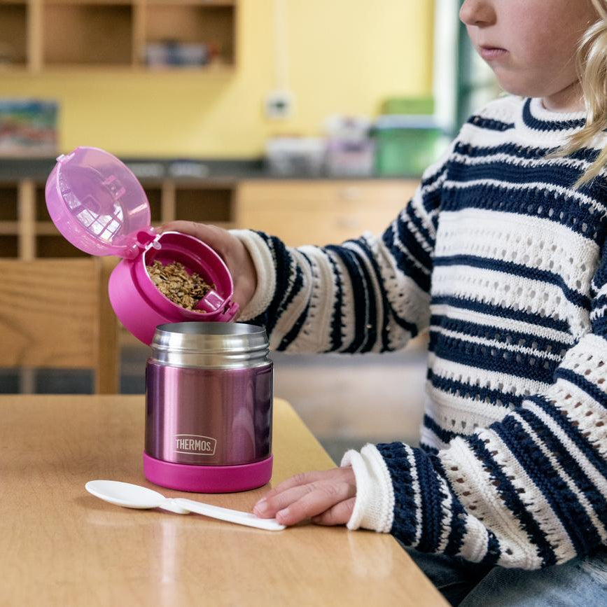 Girl pouring granola from her Thermos snack top food jar lid into the main container.