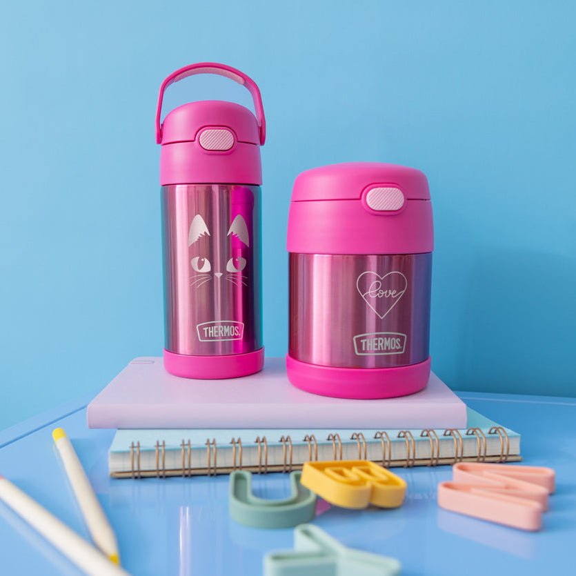 A pink Thermos water bottle and food jar on a blue surface with stationery items.