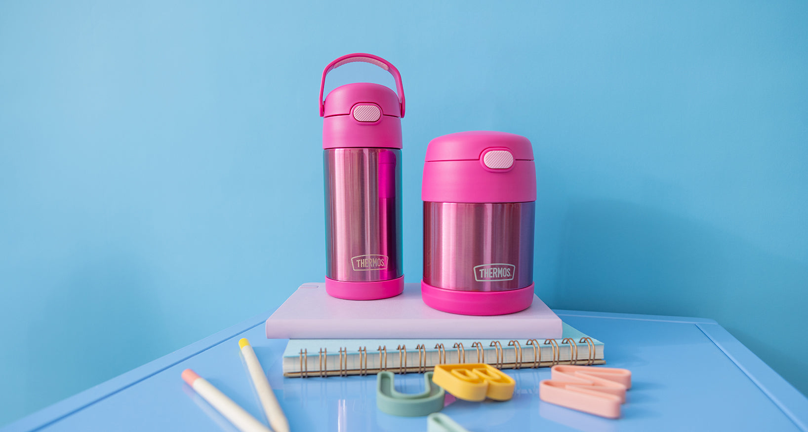 Pink thermos bottles on a blue surface with stationery items
