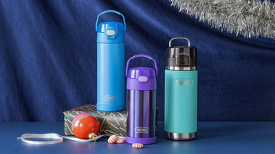 Three insulated Thermos bottles in blue, purple, and green on a blue surface with a festive tinsel border.