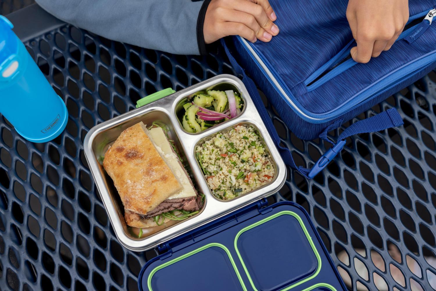 Person at a lunch table with an Icon Kids Food Storage System, a FUNtainer Water Bottle and a Blue Upright Lunch Box