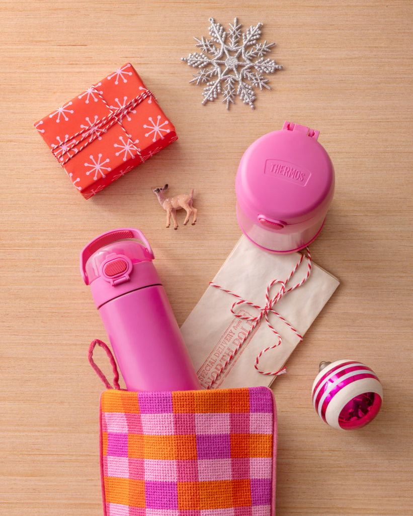 Thermos pink FUNtainer water bottle and food jar coming out of a stocking, small gift box, and decorative snowflake on wooden surface