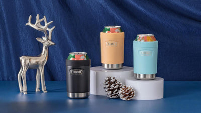 Thermos can insulators in assorted colors in front of a blue background with hanging snowflake and silver reindeer statue.