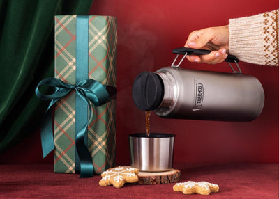 Person pouring coffee into the cap of a Thermos Beverage Bottle with handle in front of a red background.