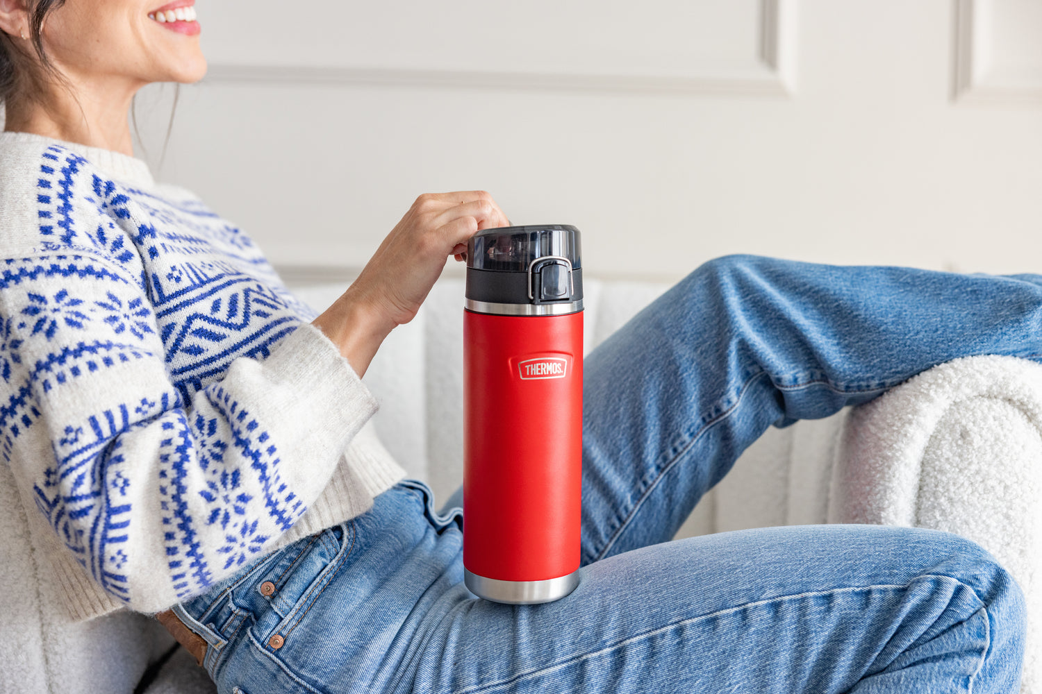 Person holding a red thermos water bottle while sitting on a couch