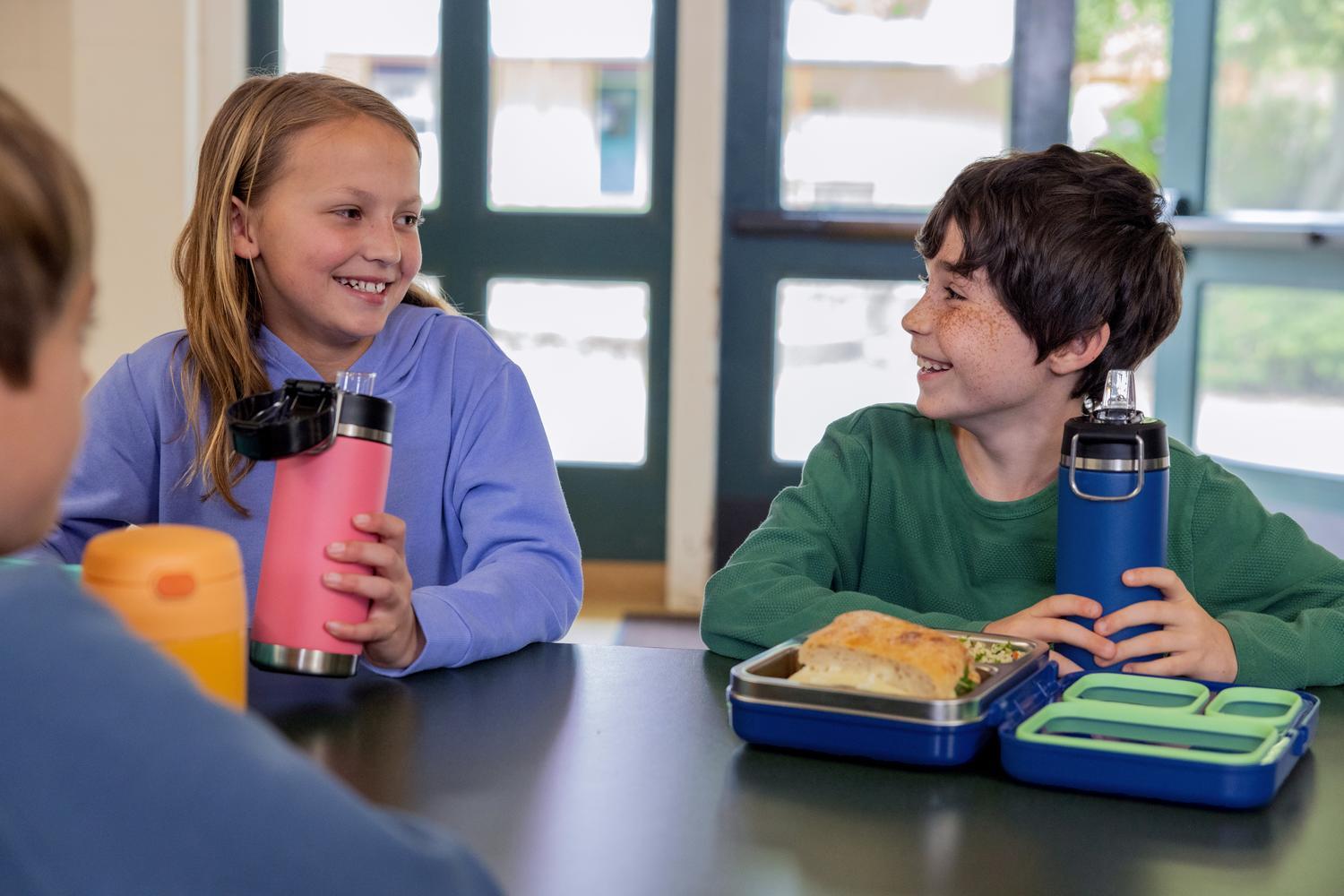 Kids in a lunchroom setting with Thermos Kids water bottles and bento box.