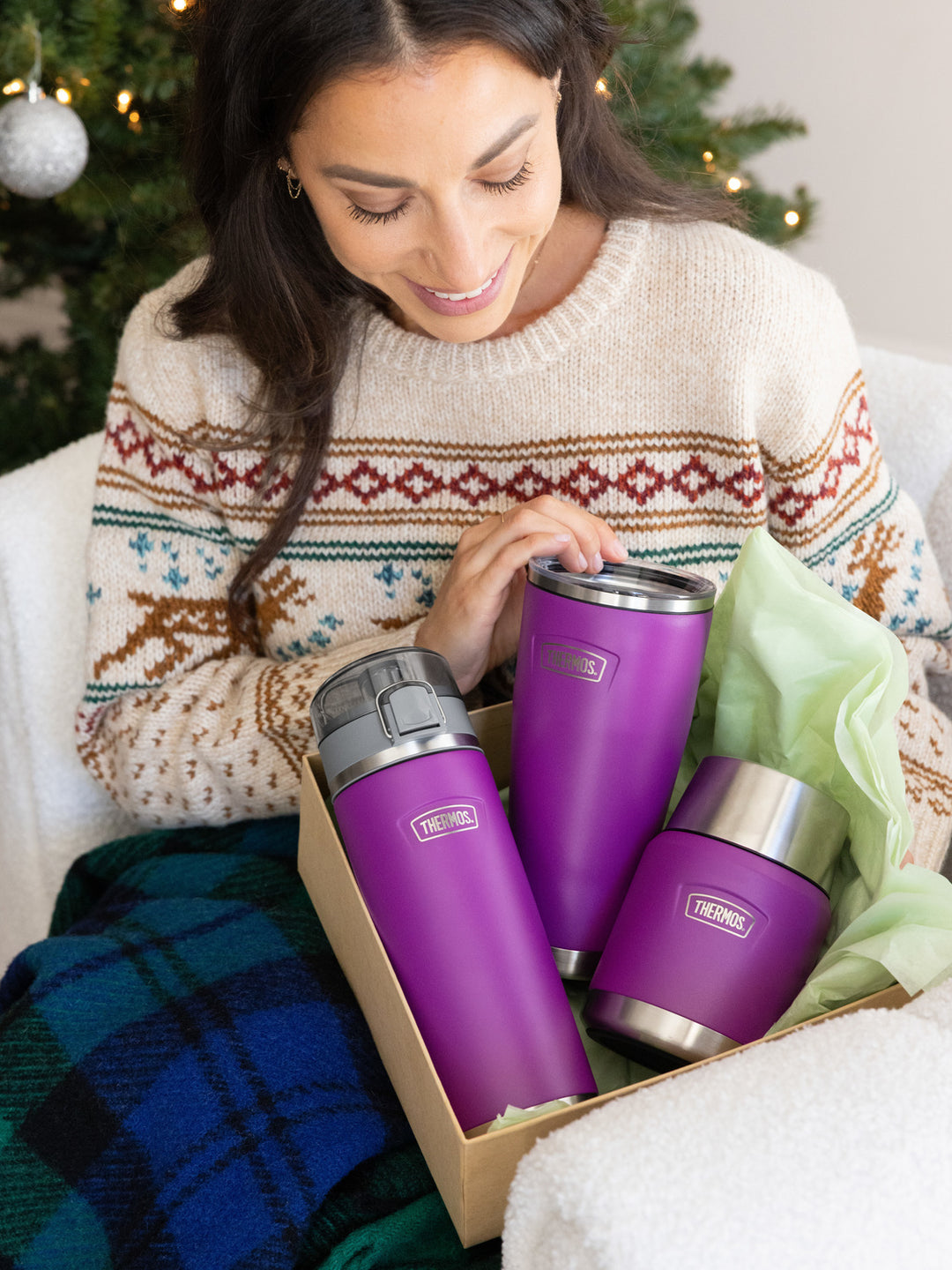 Woman holding a box of purple thermos bottles with Christmas decorations in the background