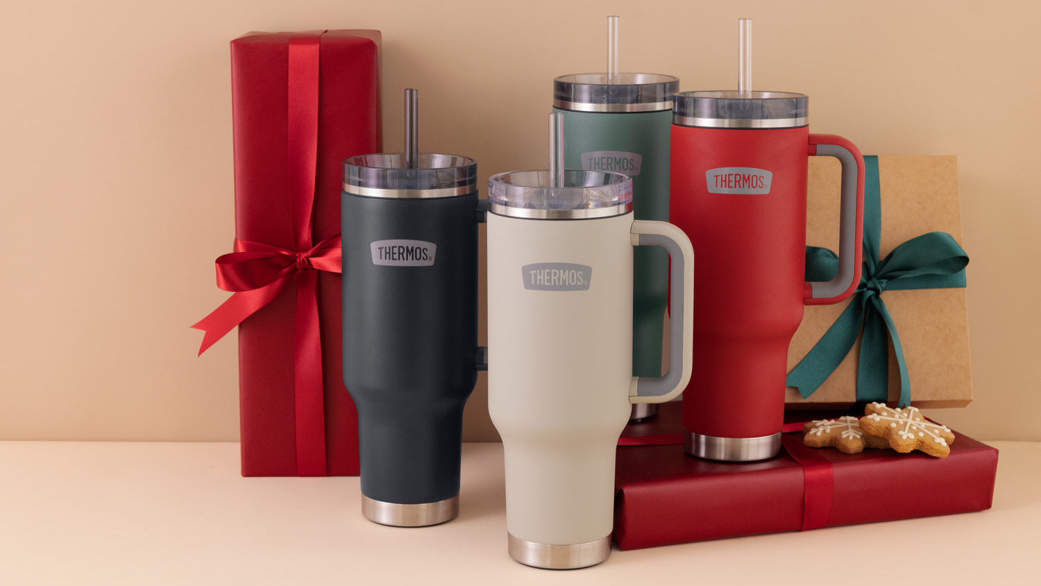 Four Thermos insulated travel mugs with straws and handles, accompanied by gift boxes on a beige background.