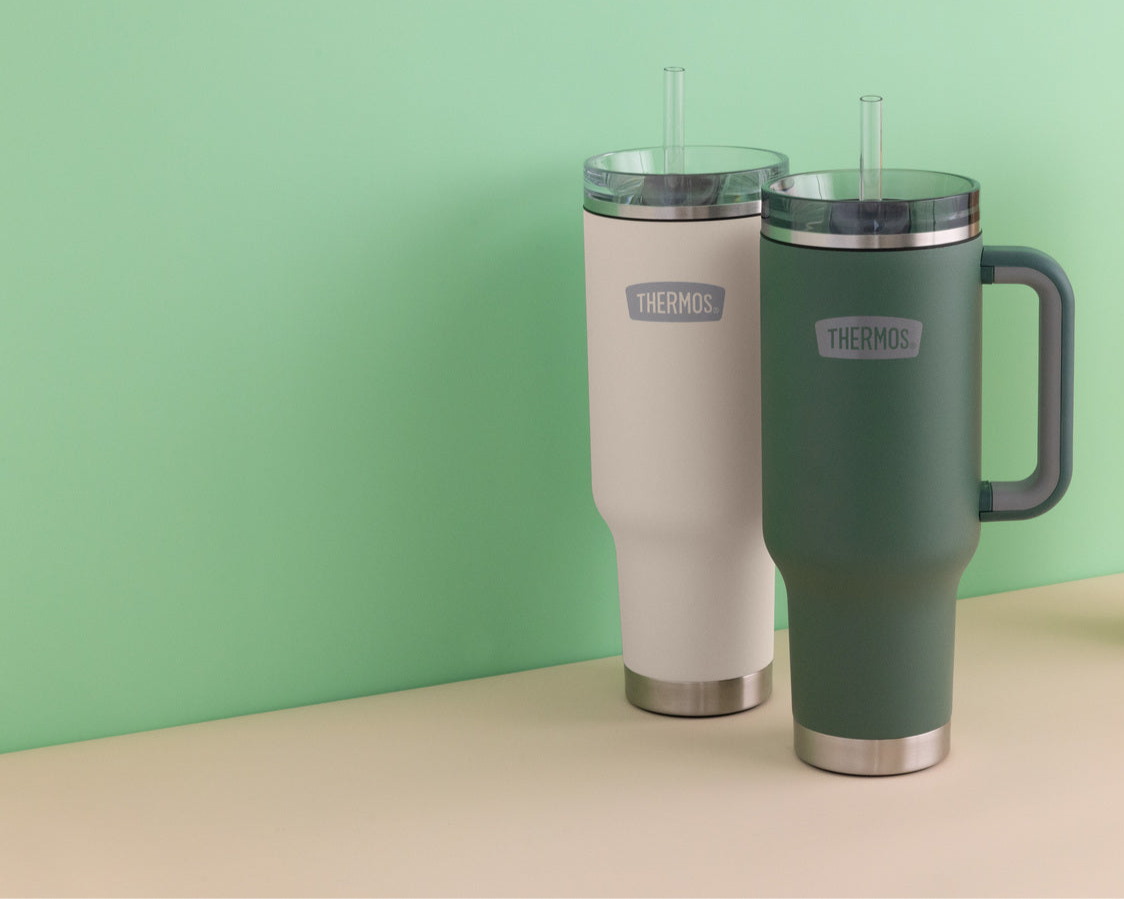 Two thermos cup holder mugs, one sandstone beige and one green, with straws on a light green background.