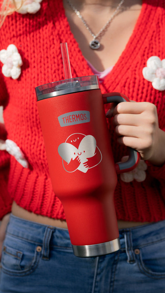 Person wearing a red sweater with white flowers holding a red tumbler.