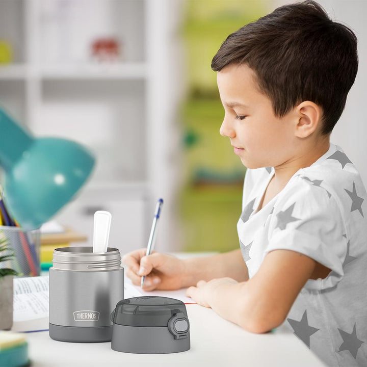 Boy sitting at table doing homework with an open 10 ounce Grey Funtainer food jar open next to him.