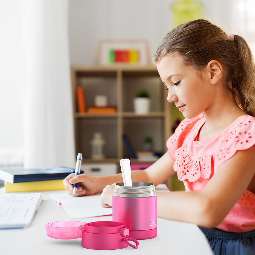 Girl sitting at table doing homework with an open 10oz Funtainer food jar with snack top open next to her. 