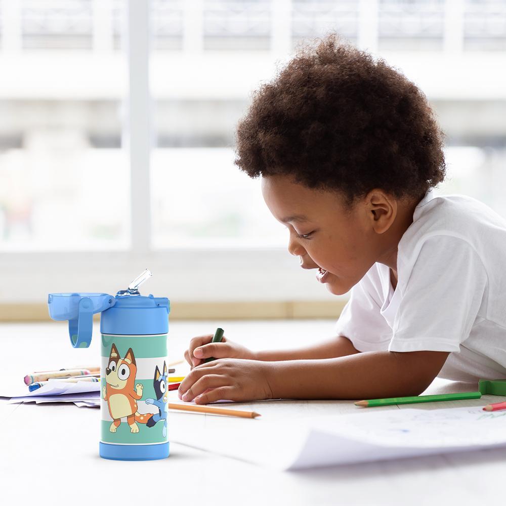 Boy sitting at a table coloring, with the 12 ounce Funtainer Bluey water bottle opened next to him.