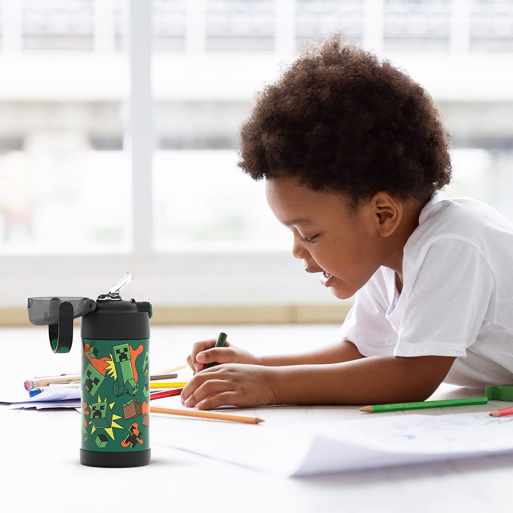 Boy sitting at a table coloring, with the 12 ounce Funtainer Minecraft water bottle opened next to him.