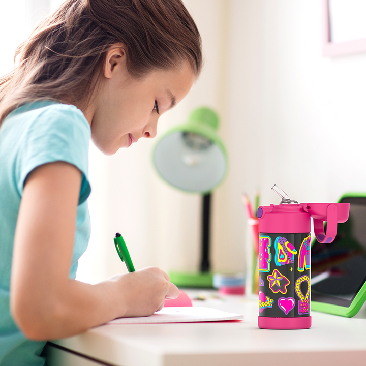 Girl sitting at a table doing homework, with a 12 ounce That Girl Lay Lay, Pink Funtainer water bottle opened next to her.