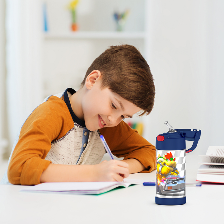 Boy sitting at a table doing homework, with the 12 ounce Funtainer Mario Kart water bottle opened next to him.